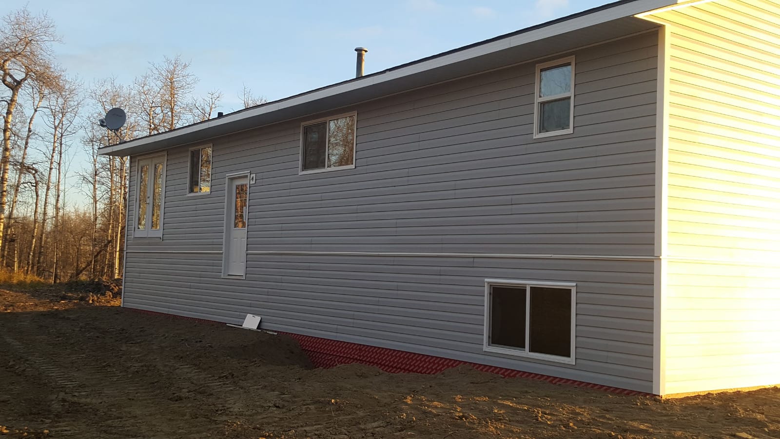 The same house re-sided in grey lap siding, standing on bare earth.
