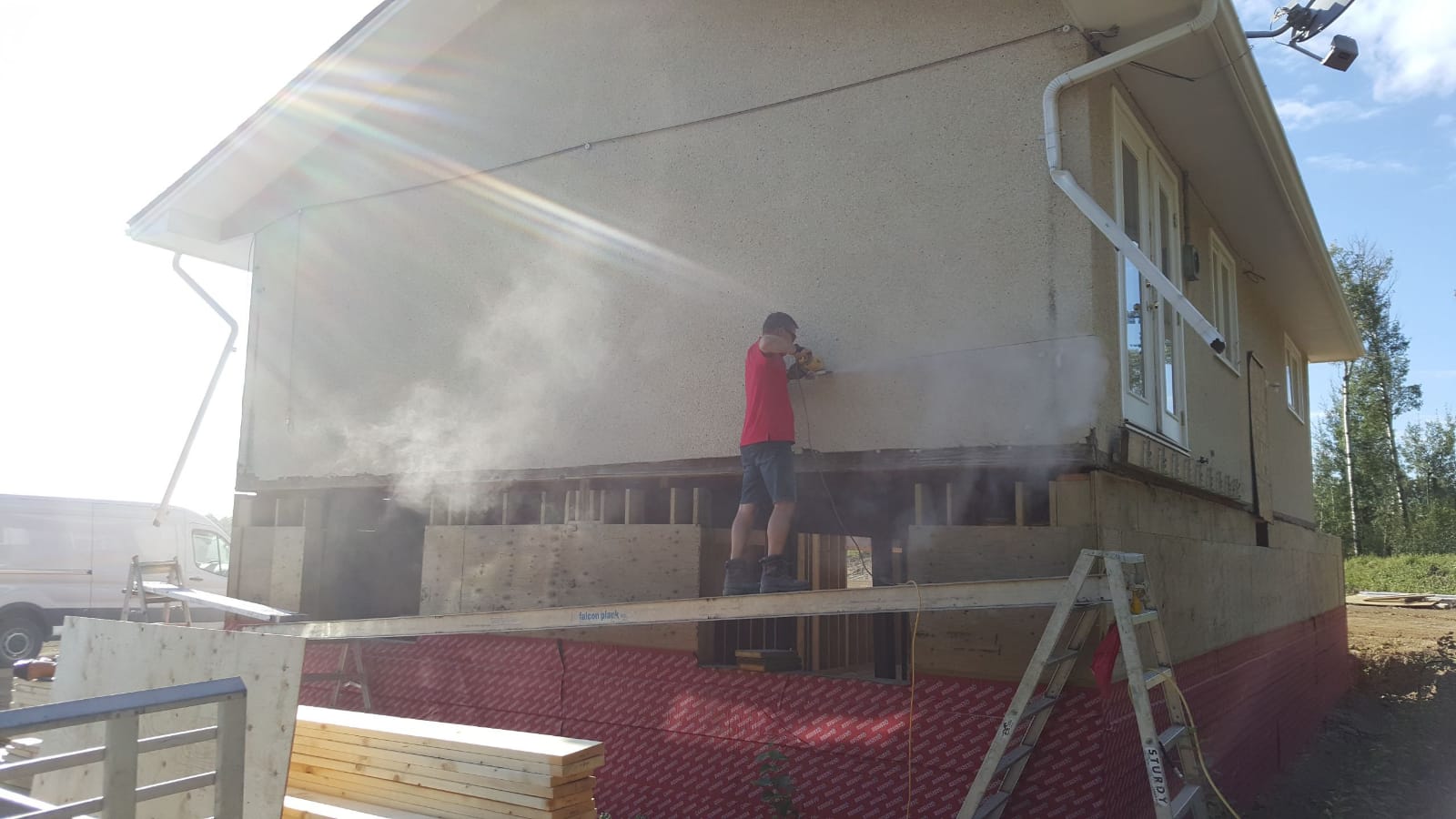 A worker on staging stripping the old stucco from a house down to the sheathing.