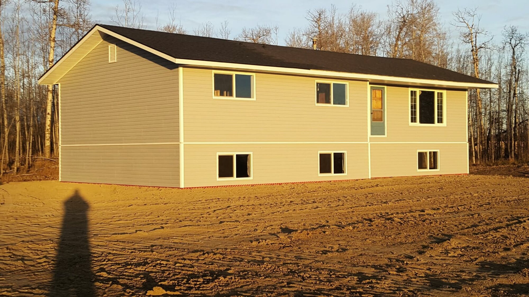 A finished house standing on raw, unlandscaped earth at golden hour in Red Deer County.