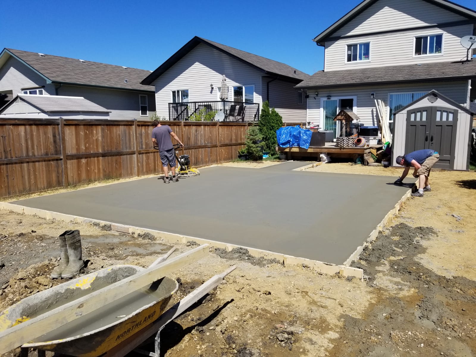 A crew screeding a freshly poured concrete pad on excavated ground.